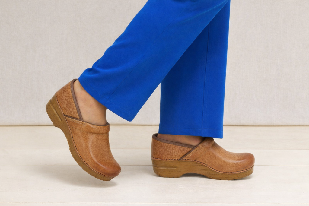 Classic Dansko professional clogs in tan leather styled with vibrant blue trousers for a unique and bold fashion statement